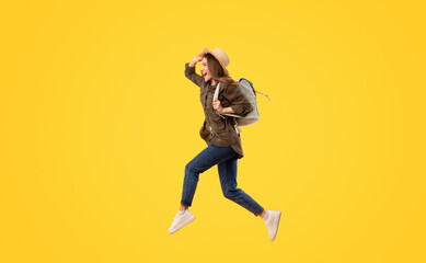 Fototapeta na wymiar Happy Tourist Lady With Backpack Jumping Over Yellow Background