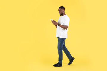 African American Guy Using Cellphone Texting Walking Over Yellow Background