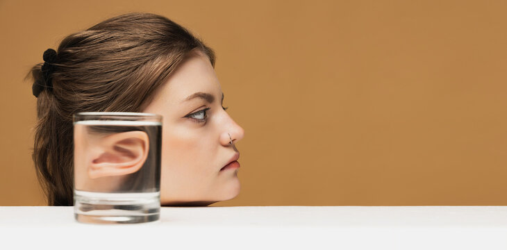 Fototapeta Creative art photography. Stylish girl's face through wine glass over sand color background. Object distortion, optical illusion. Minimalistic contemporary art.