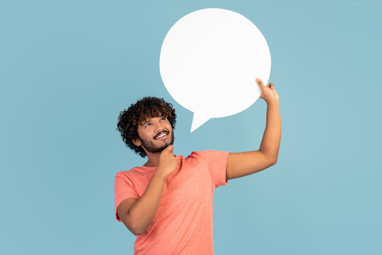 Pensive indian man holding blank speech bubble on blue, thinking