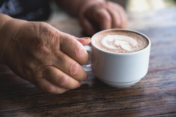 Seniour old woman is holding tasty cappucino with art latte.