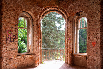 Obraz premium Abandoned red brick building windows without glasses, view from inside to green trees