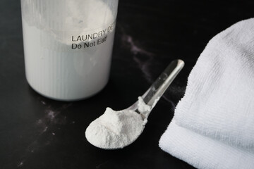 Washing powder in plastic spoon and towel on black background 