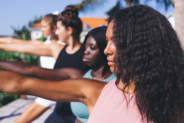 Female yogi in sportswear teaching asanas diverse friends during together balance practice, group of concentrated biracial persons training in teamwork - keeping body positive and vitality wellness