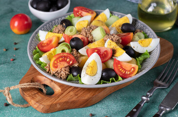 French salad Nicoise with canned tuna, boiled potatoes, egg, black olives, cucumbers, tomatoes and lettuce on gray plate
