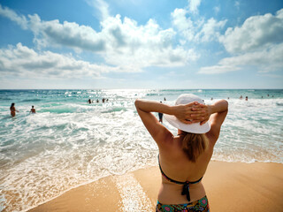 Tanned girl with a white hat, relaxes on the beach looking at the sea on a sunny summer day, in the...