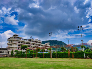 Image of a building with clouds in sky and hills in background. Chandra Mahal Garden. Aravalli Hills