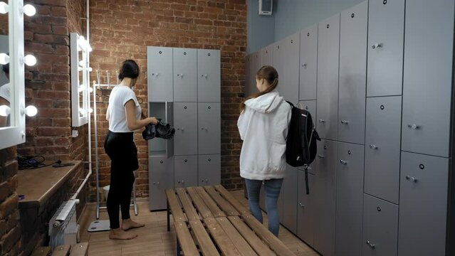 Woman comes into dressing room giving high five to greet friend opening locker to put things. Ladies meet in fitness club before training slow motion