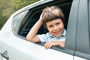 Cheerful caucasian small kid go on vacation by car and looks out window, enjoys trip and weekend, outdoor