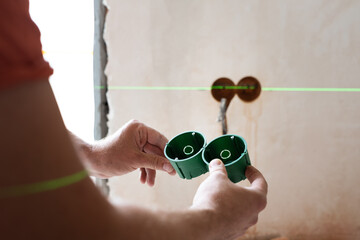 Electrical wiring work on the wall using laser level device. Man holding two round plastic...