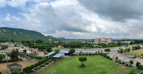 Image of a building with clouds in sky and hills in background. Chandra Mahal Garden. Aravalli Hills