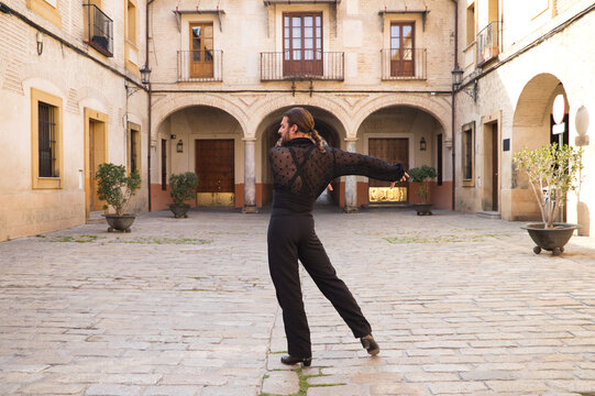 middle-aged flamenco man with long hair dancing flamenco in a square with columns and balconies in seville, spain. Feel the passion. Flamenco dance concept cultural heritage of humanity.