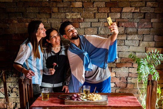 Familia  Haciendo Video Conferencia En La Previa Antes Del Mundial De Futbol, Con Picadas Y Cervezas,  Con Los Colores Celeste Y Blanco, Luz Natural, Riendo.