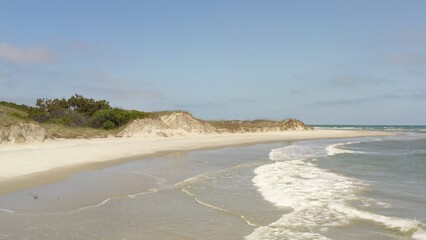 Deserted beach with sand dunes and waves breaking on shore