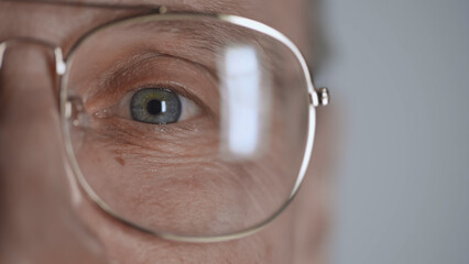 cropped view of mature man with blue eye and eyeglasses looking at camera isolated on grey