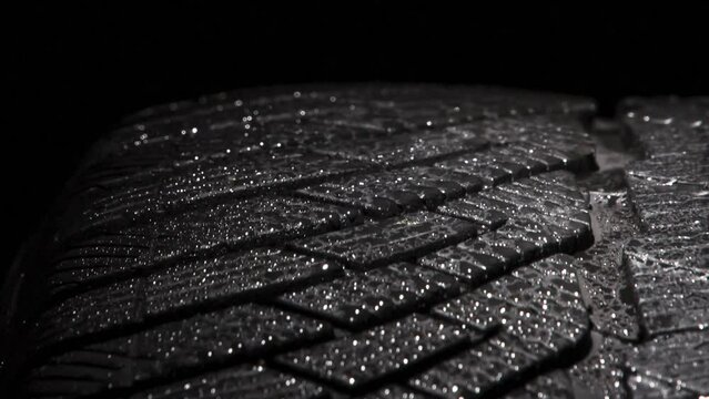 Rotation Wet Automobile Tire. The geometric pattern of the wheel in water droplets slowly rotates towards the viewer. Drops sparkle on the black rubber on a black background
