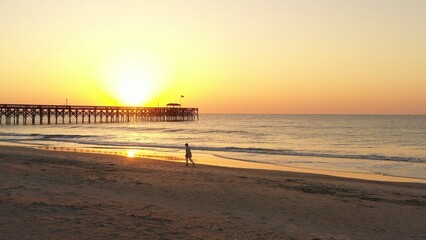 Sun rising over peaceful ocean with fishing pier on the beach