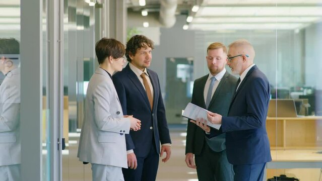 Young businesswoman giving documents to senior manager and then shaking hands with him and male colleagues while working on partnership agreement in office