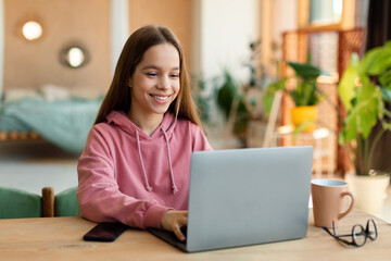 Distance education concept. Happy teen girl sitting at desk, using laptop and watching lecture or webinar