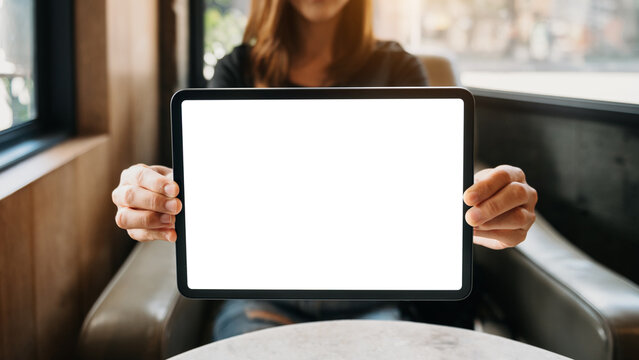 Mockup image of a beautiful woman holding and showing a tablet and smartphone with blank white screen while sitting on sofa at cafe.