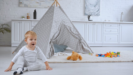 excited toddler boy sitting near baby wigwam and toys on carpet © LIGHTFIELD STUDIOS