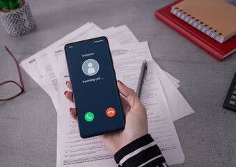 Unknown number calling. Phone call from stranger. Person holding mobile and smartphone in office. Unexpected call disturbs at work. - obrazy, fototapety, plakaty