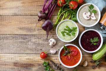 Autumn set of different vegetable soups. Healthy food. Vegan hot cream soups (tomatoes, mushrooms, beets, green beans) on rustic wooden table. View from above. Copy space.