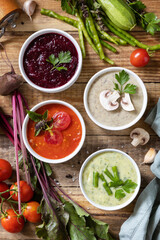 Autumn set of different vegetable soups. Healthy food. Vegan hot cream soups (tomatoes, mushrooms, beets, green beans) on rustic wooden table. View from above.