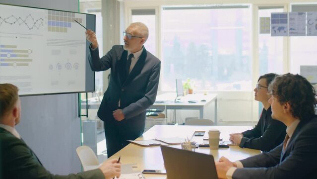Senior businessman using digital whiteboard while giving presentation to team on corporate meeting in office