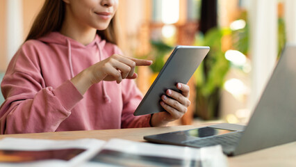 Web based schooling. Female teenager using tablet and laptop for online education, sitting at desk at home, cropped