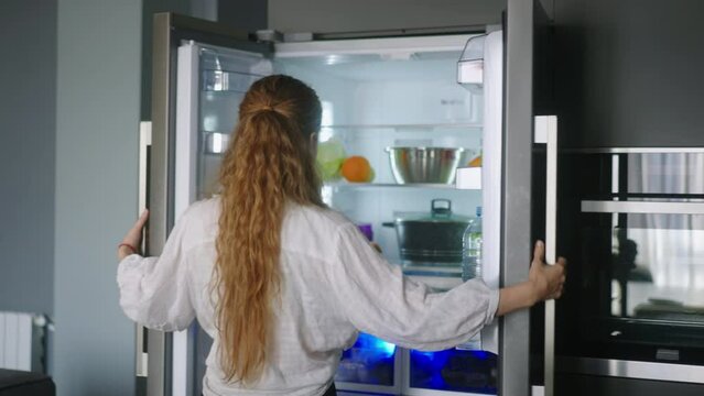 Young woman taking an orange from fridge throwing it up. Girl getting a fruit from refrigerator. Female having something healthy for snack. Caucasian woman is about to cut orange. Girl cutting orange
