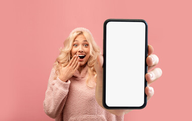 Surprised young woman showing big blank smartphone at camera