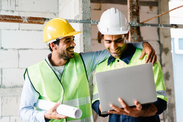 Civil Engineer and Contractor working on building site wearing safety hardhat and vest and using laptop computer