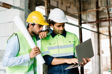 Civil Engineer and Contractor with safety hardhat using laptop computer while standing and working side by side on a building site