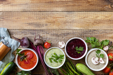 Autumn set of different vegetable soups. Healthy food. Vegan hot cream soups (tomatoes, mushrooms, beets, green beans) on rustic wooden table. View from above. Copy space.