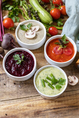 Autumn set of different vegetable soups. Healthy food. Vegan hot cream soups (tomatoes, mushrooms, beets, green beans) on rustic wooden table.