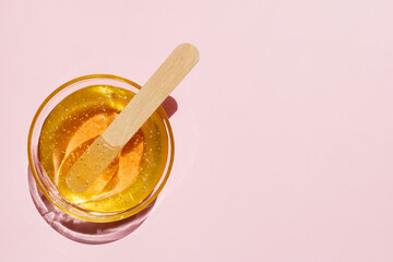 Liquid yellow sugar paste, wooden spatula on a pink background. Removing unwanted hair. Sugaring. Depilation. Epilation. Beauty. Top view. Place for text. - obrazy, fototapety, plakaty