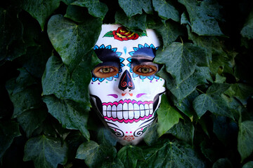 Máscara de calavera mexicana del Día de los Muertos con ojos humanos sobre fondo vegetal.