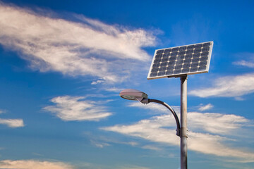 Placa de energía solar sobre una farola de alumbrado público con fondo de cielo nuboso.