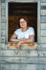 Portrait. adult pretty woman in glasses with short hair looks out of the window of a wooden house