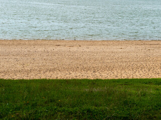 Water, sand and grass stripes on a beach. Abstract natural colors on a shoreline. Blue, yellow and green tones of the different ground materials. Landscape background at a summer day.