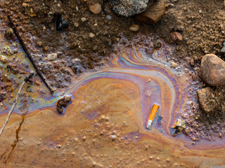 Oil spill in the nature. Pollution in the water and on the sand. A cigarette butt is lying in the environment. Humans destroy the planet with their carelessness and ignorance. Spectral colors of light