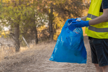 Detalle de hombre guardabosque caucásico, metiendo botella de plástico en bolsa de basura en la montaña. Fotografía horizontal con espacio para texto. - obrazy, fototapety, plakaty