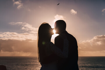 silhouettes of kissing newlyweds on sunset and ocean background.