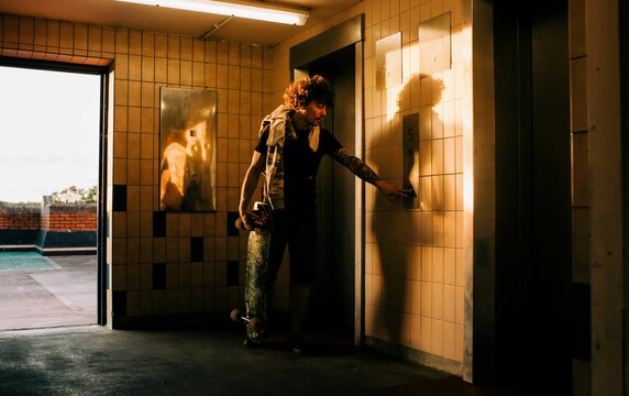man pressing the elevator button in the city with his skateboard