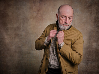 casual studio portrait of a bearded senior man in deep thought or contemplation against grunge wall
