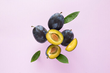 Flying in air fresh ripe whole and cut blue plums with leaves on the purple background. Close-up.
