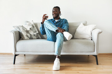 African American Guy Using Smartphone Sitting On Couch At Home