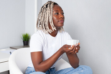 Mujer negra sujetando una taza sentada en su habitación relajada. Lifestyle. 