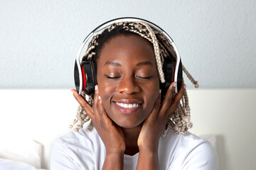 Mujer negra sonriente escuchando música con auriculares en la habitación de su casa. Lifestyle.